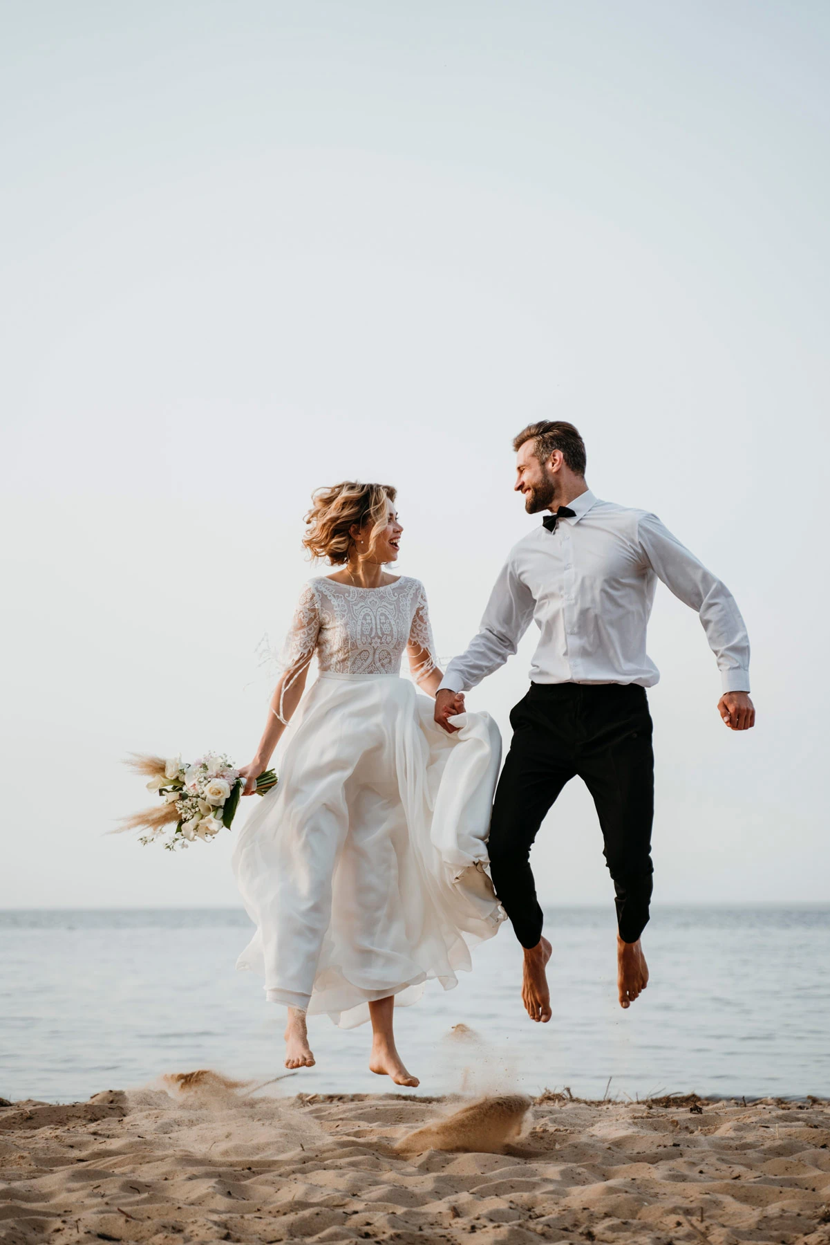 Brautpaar springt an Strand Hochzeitslocation von Marrycation in die Luft